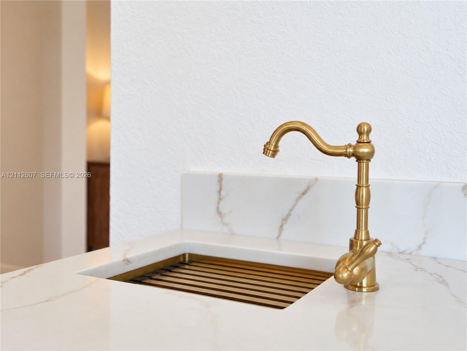 Integrated stone-finish countertop with a coordinating backsplash, featuring a custom metal-finish sink basin and a decorative brass-finish gooseneck 