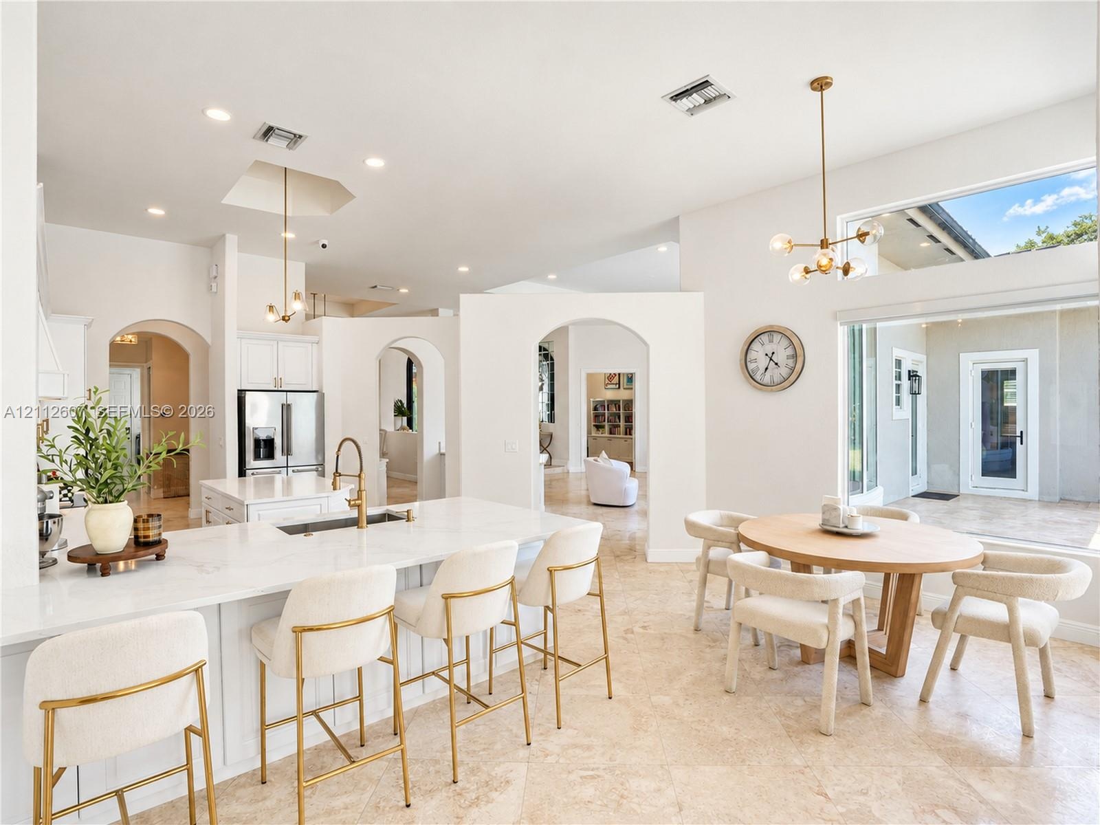 Open-concept interior featuring high ceilings, stone flooring, a center island with stone countertop, brass-finish pendant lighting, and arched archit