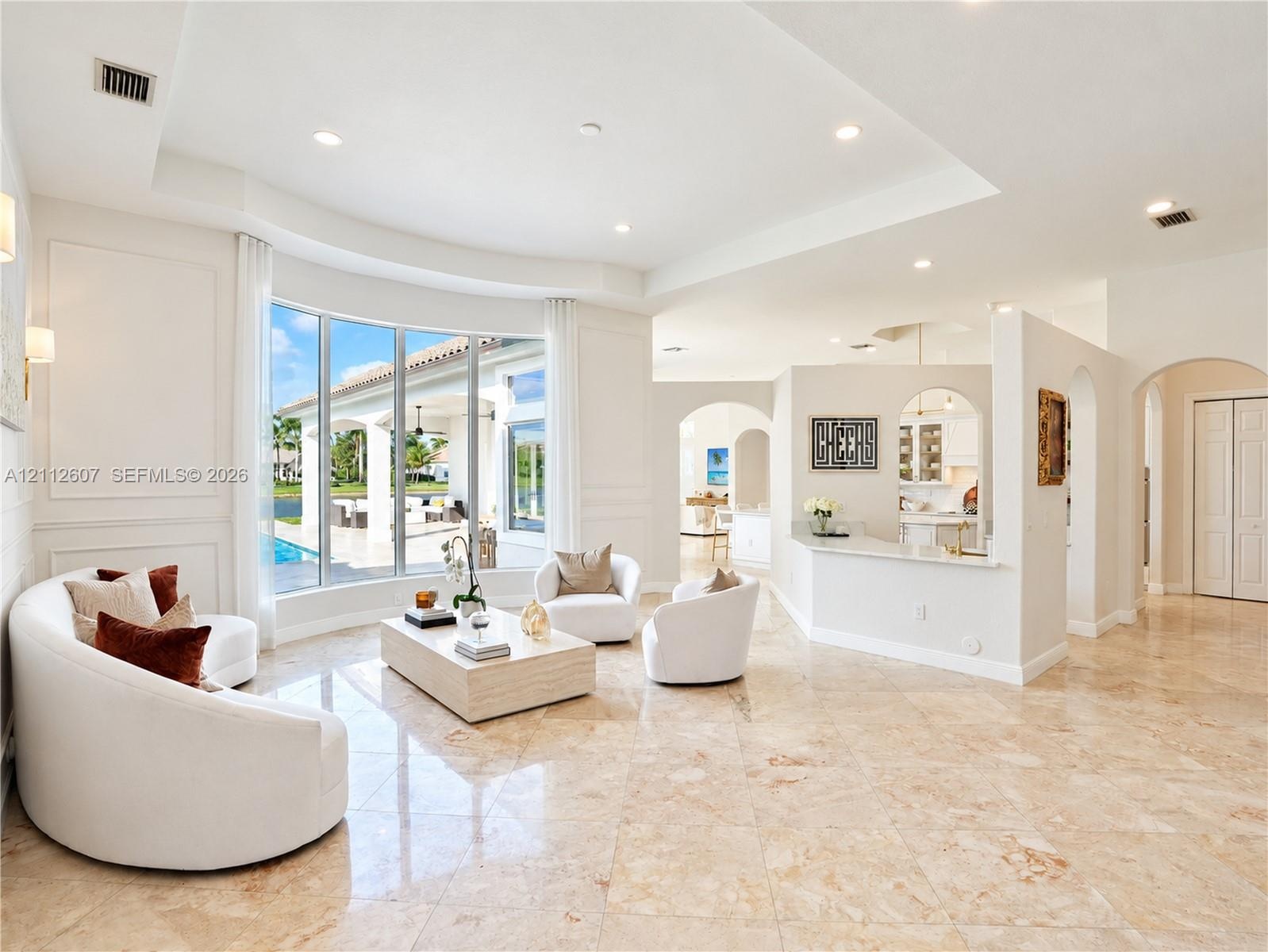 Spacious living area featuring polished stone flooring, a tray ceiling, curved bay windows, and a built-in partition wall with an integrated breakfast