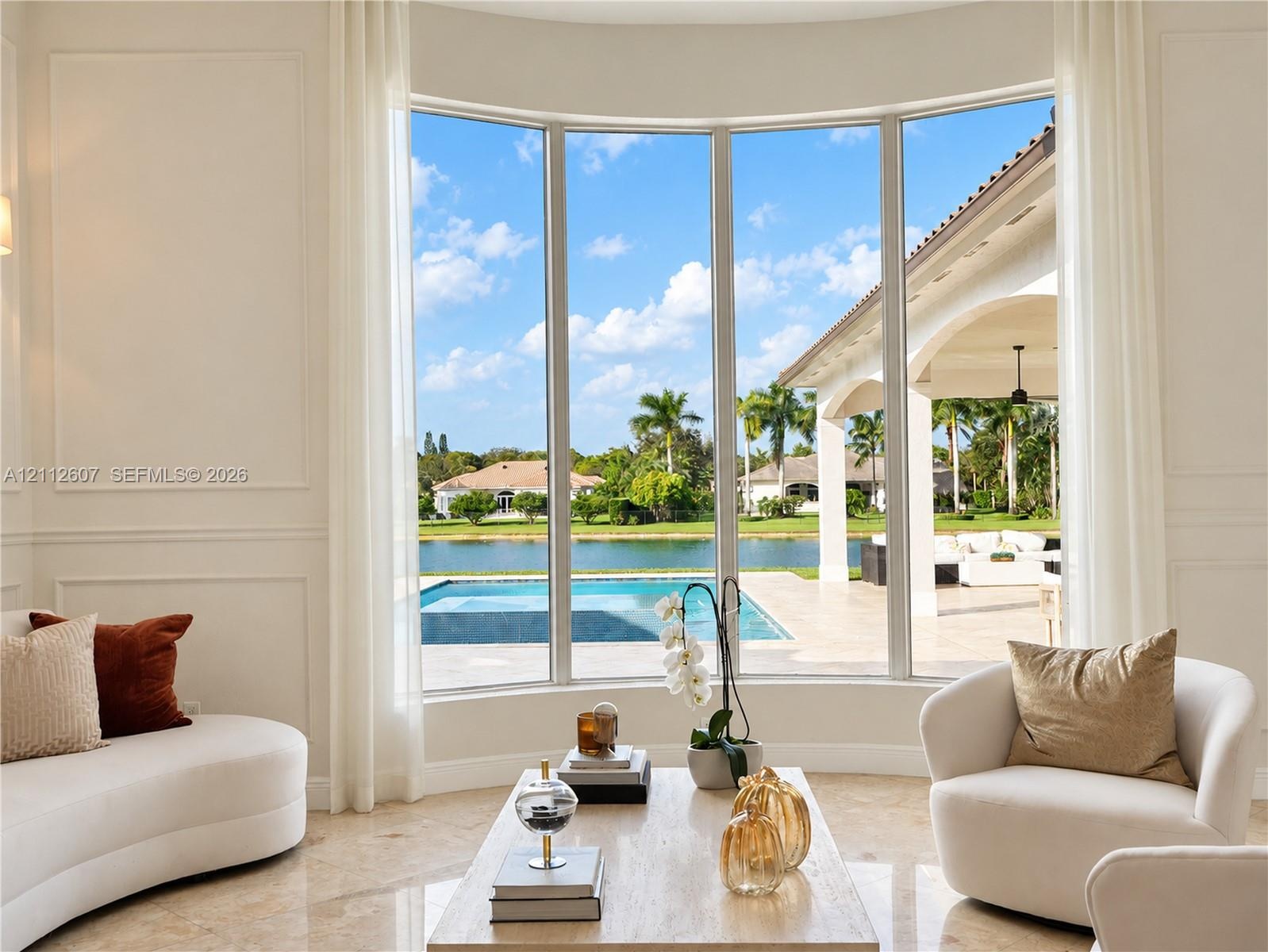 Curved floor-to-ceiling windows, wall paneling, and polished stone flooring, featuring exterior access to a covered lanai, private pool, and water fro