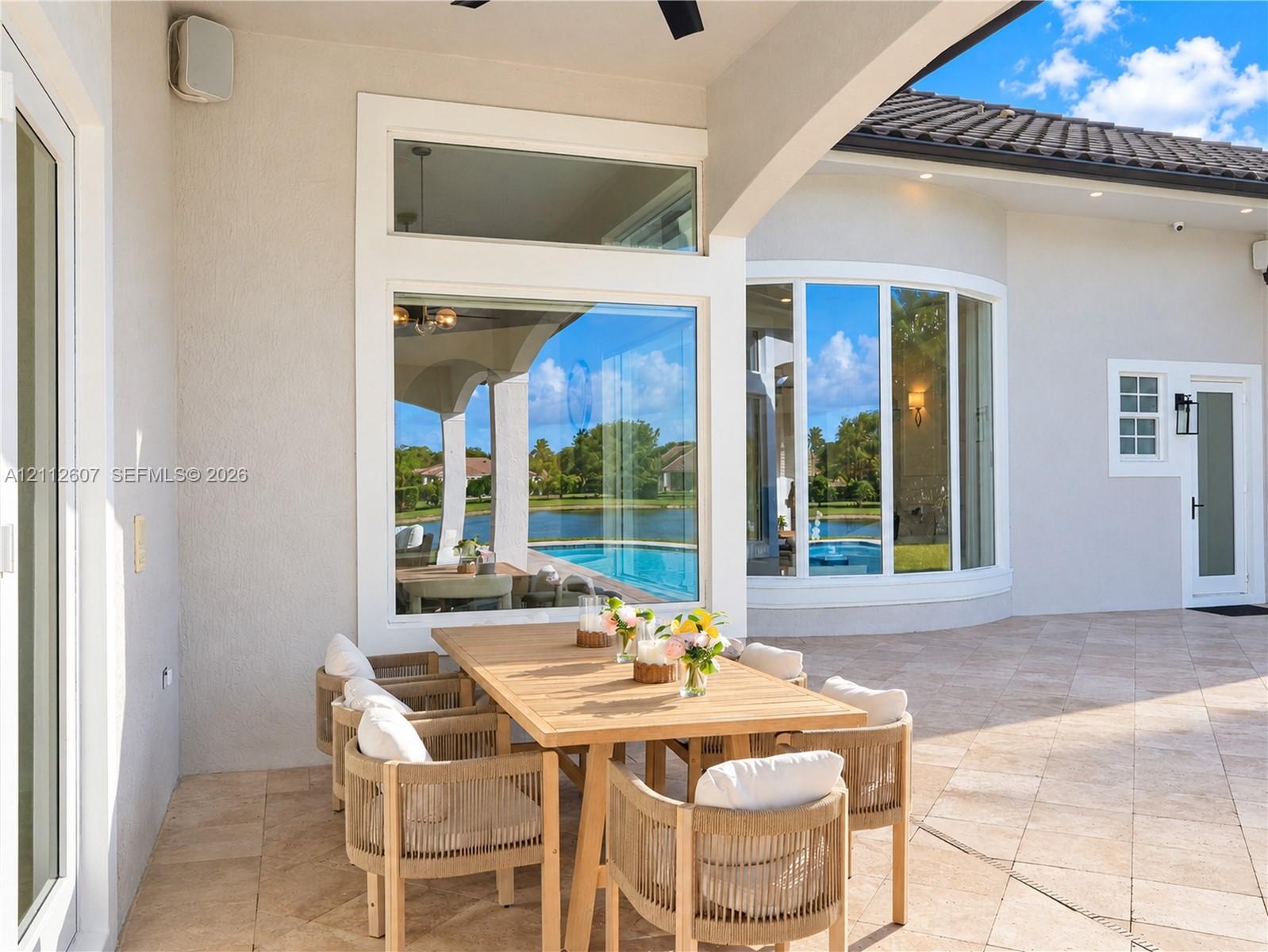 Covered lanai featuring neutral stone tile flooring, an integrated ceiling fan, expansive glass picture windows, and a curved architectural wall detai