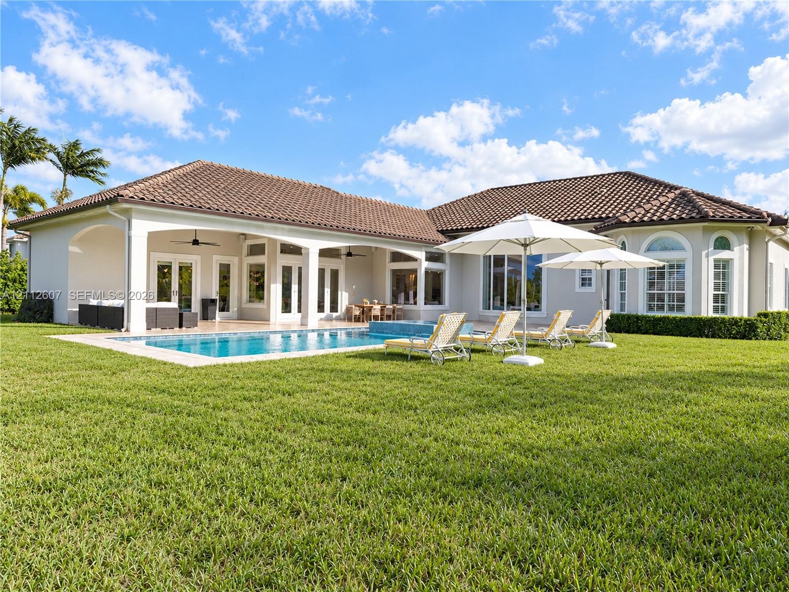 Rear exterior featuring a tile roof, covered patio with recessed lighting, in-ground pool with integrated spa, and expansive lawn