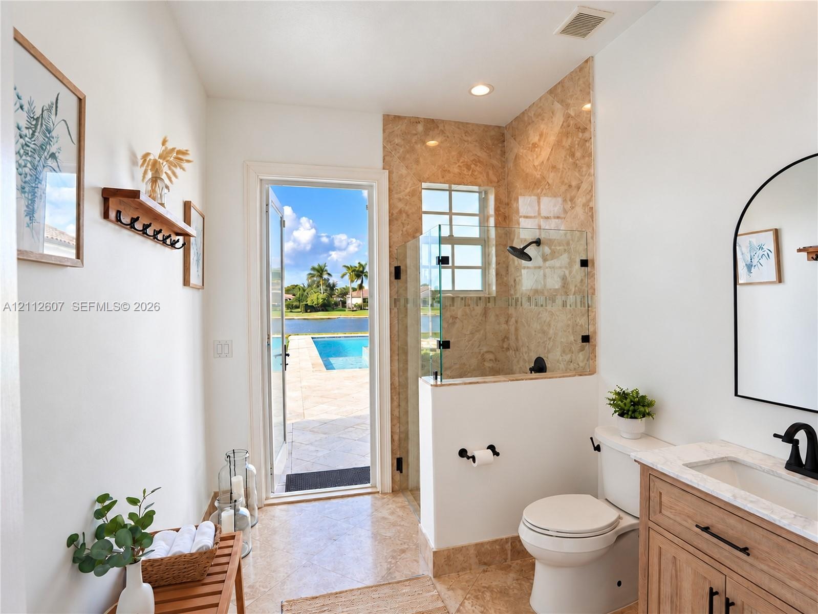 Bathroom featuring a walk-in shower with stone tile surround, glass enclosure, and matte black fixtures, paired with a wood-finish vanity topped with 