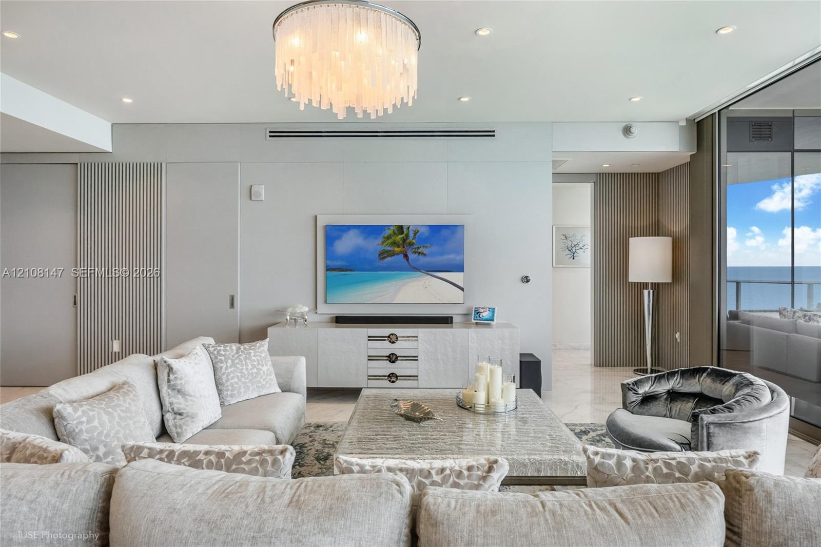 Living space featuring a multi-tiered crystal chandelier, vertical wall paneling, stone flooring, and floor-to-ceiling glass paneling