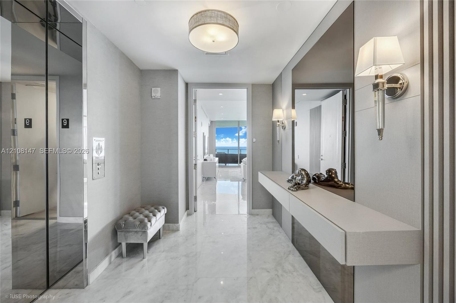 Foyer featuring polished stone flooring, custom wall-mounted floating console, mirrored wall panels, decorative wall sconces, and recessed drum ceilin