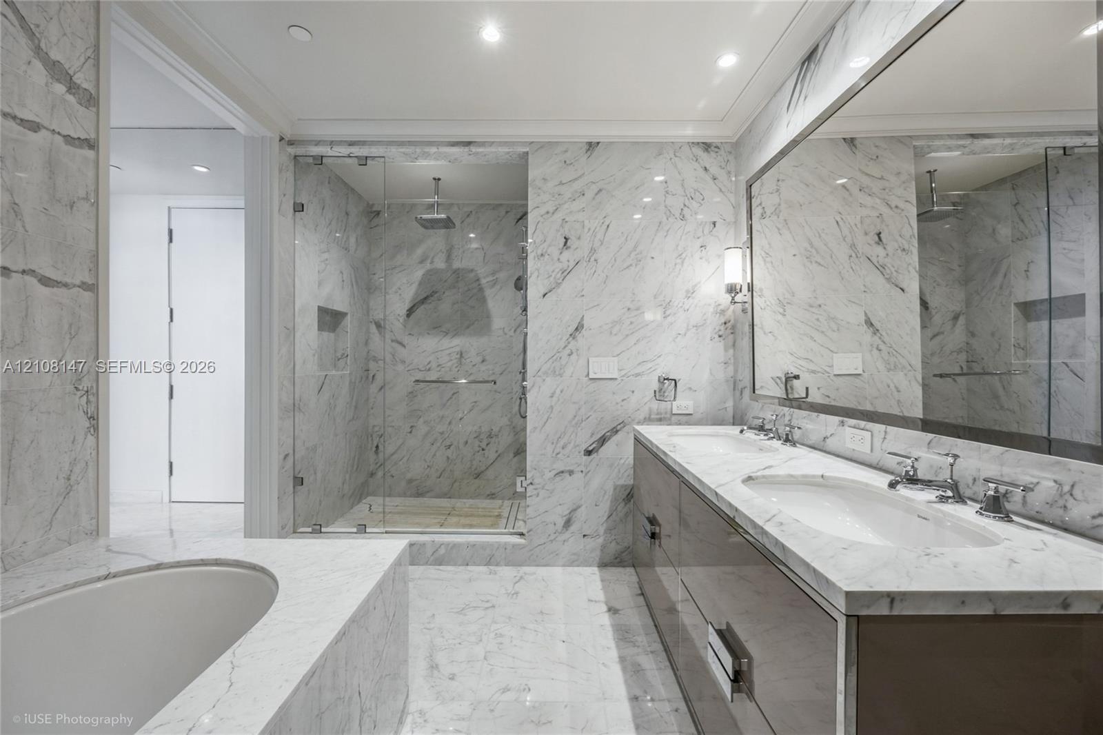 Bathroom featuring extensive stone-surround, frameless glass-enclosed shower with built-in recessed shelving, integrated soaking tub, custom dual-sink