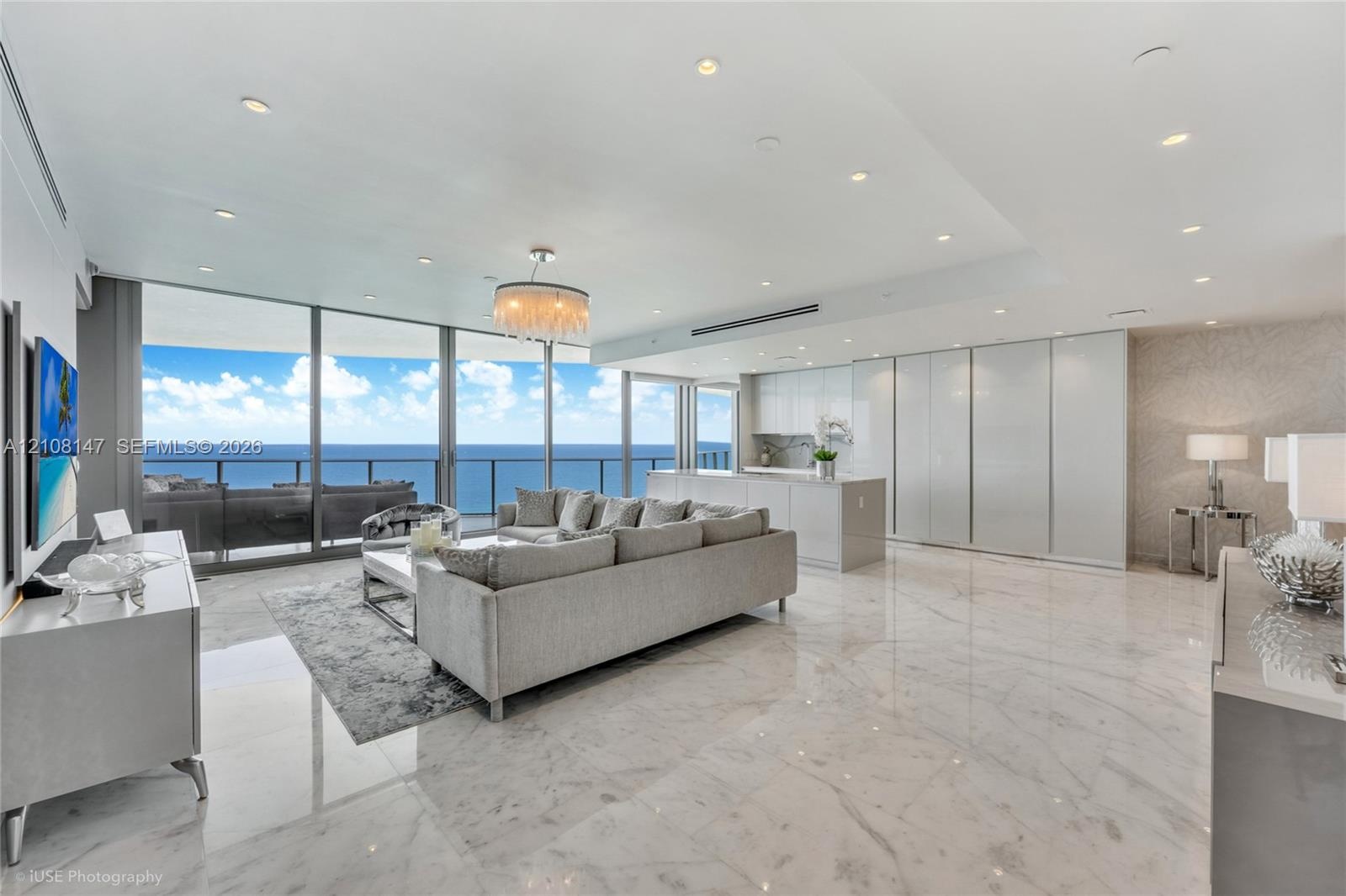 Open-concept interior featuring floor-to-ceiling glass panel walls, light-toned stone-finish flooring, recessed lighting, sleek high-gloss cabinetry, 