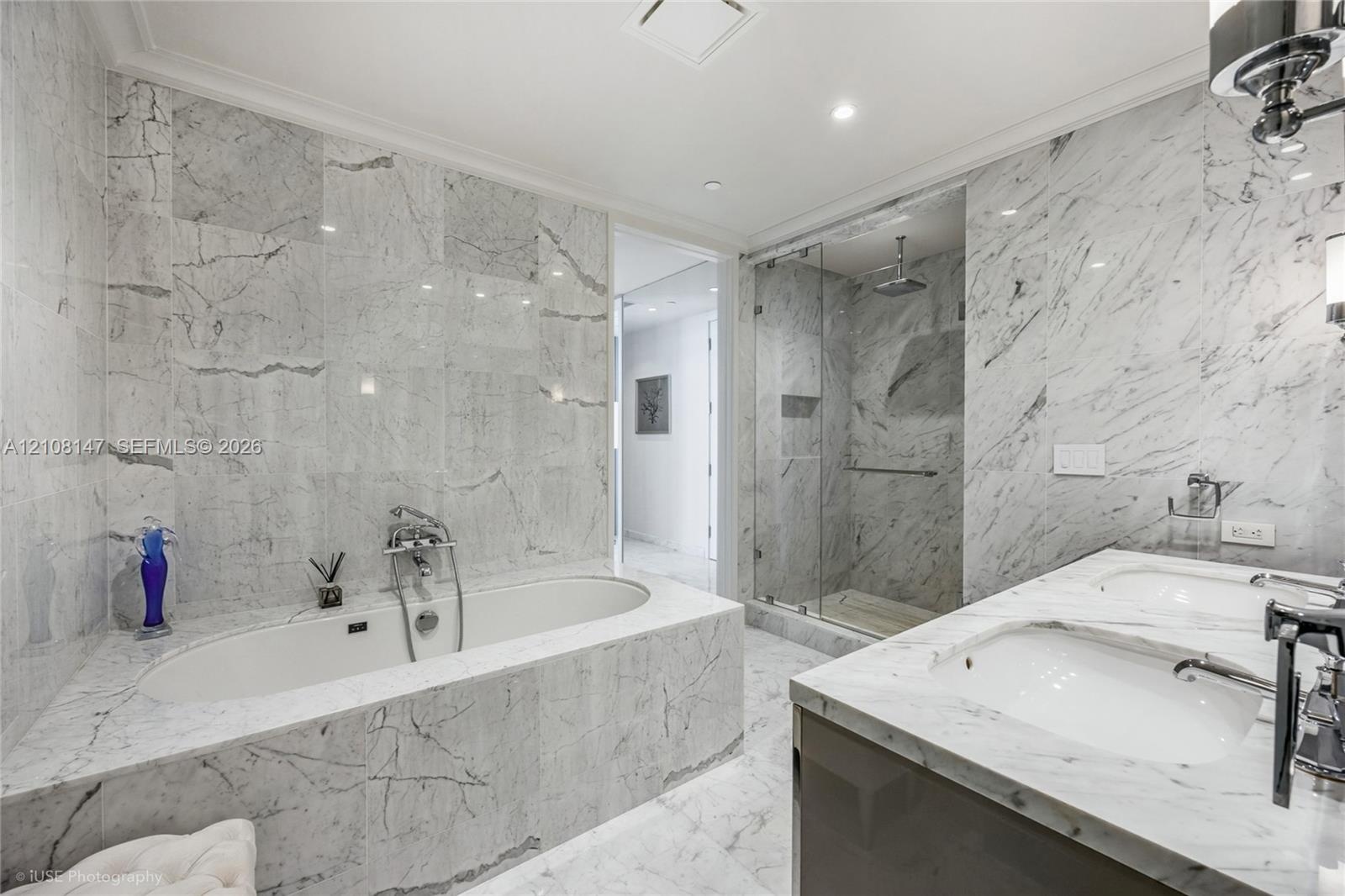 Bathroom featuring floor-to-ceiling stone tile surround, soaking tub with wall-mounted hardware, glass-enclosed walk-in shower, and dual-basin vanity 