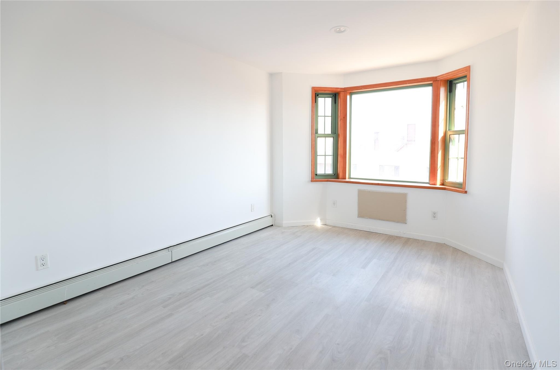 Room featuring wood-finish flooring, a three-panel bay window with wood-trim framing, and neutral wall tones