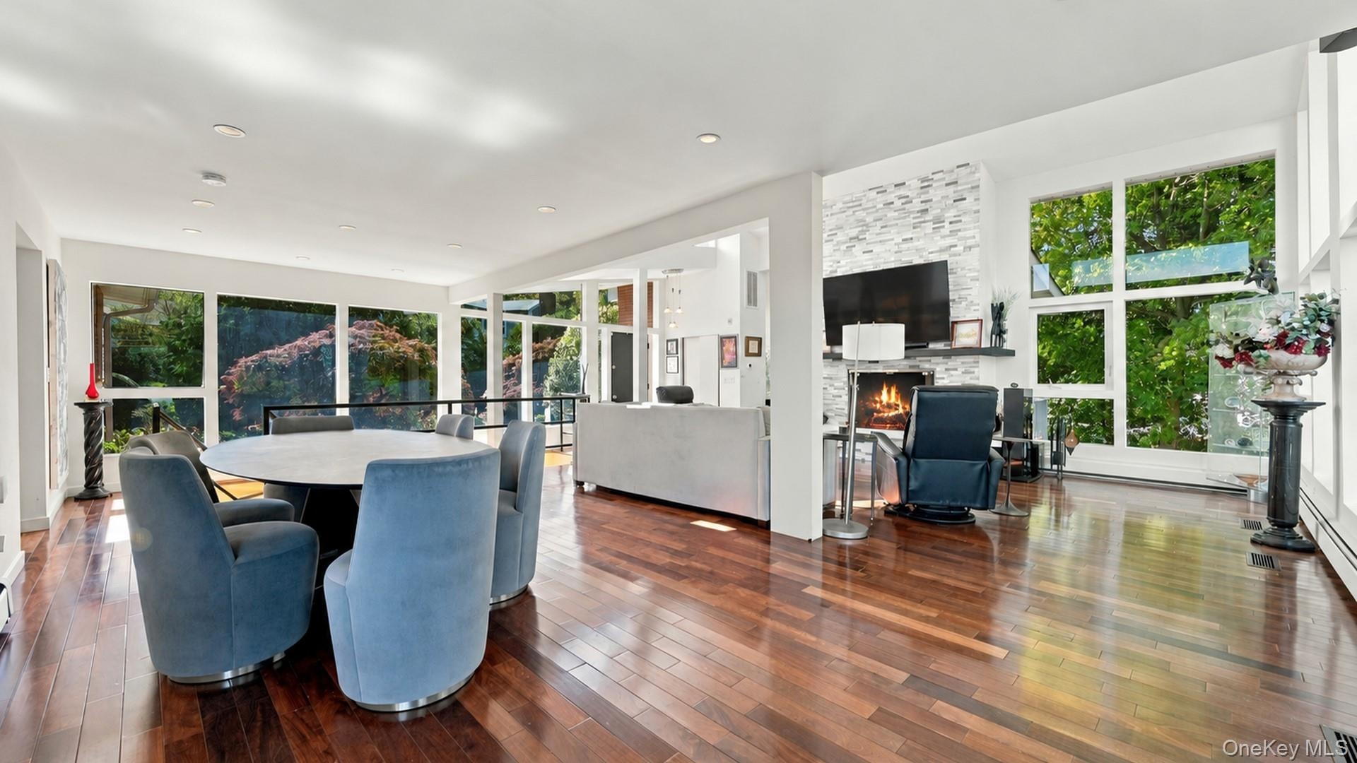 Open-concept interior featuring hardwood flooring, floor-to-ceiling windows, recessed lighting, and a floor-to-ceiling stone-veneer fireplace