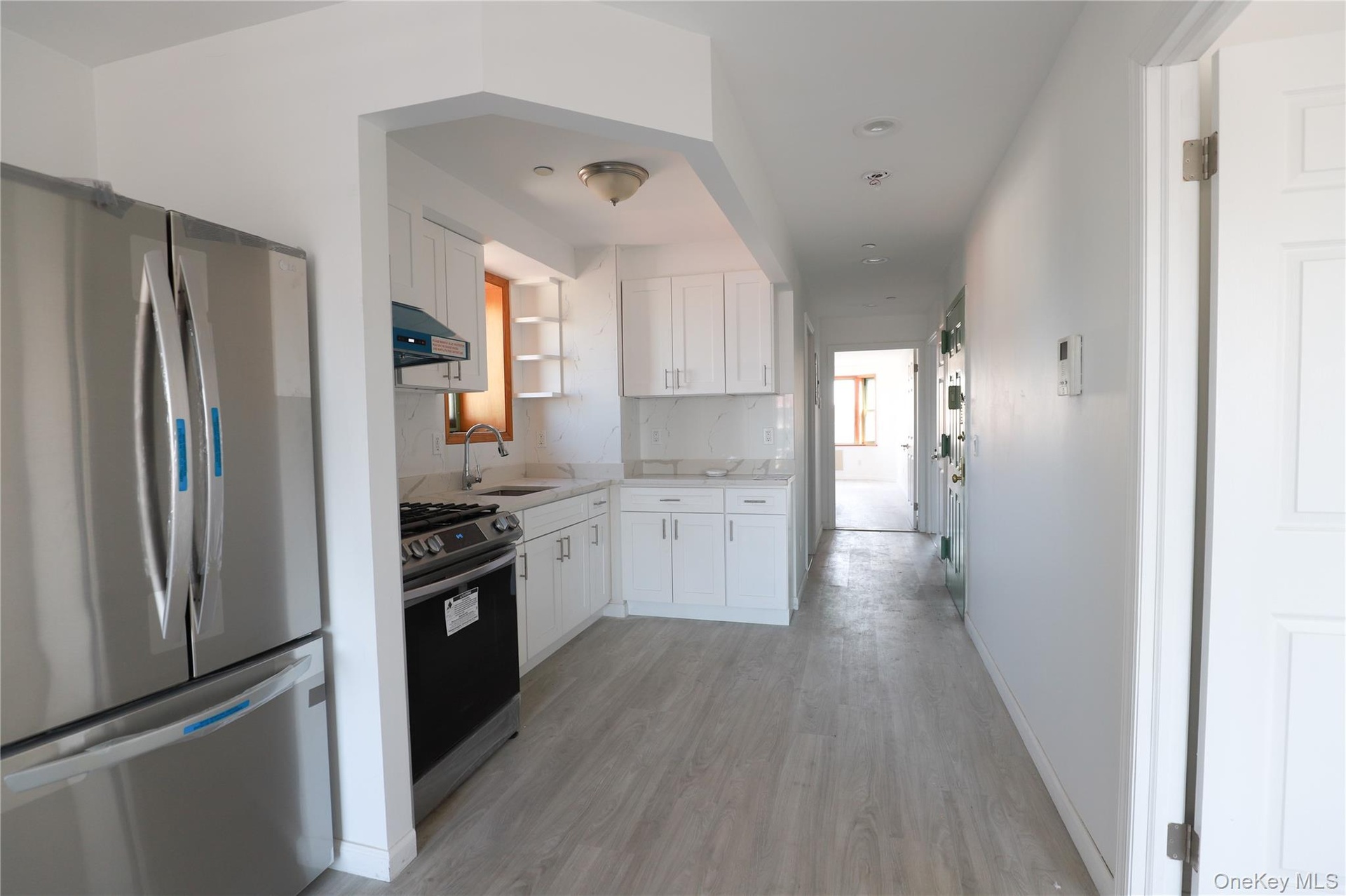 Kitchen featuring stainless steel refrigerator and range, white cabinetry, solid-surface countertops, and wood-finish flooring