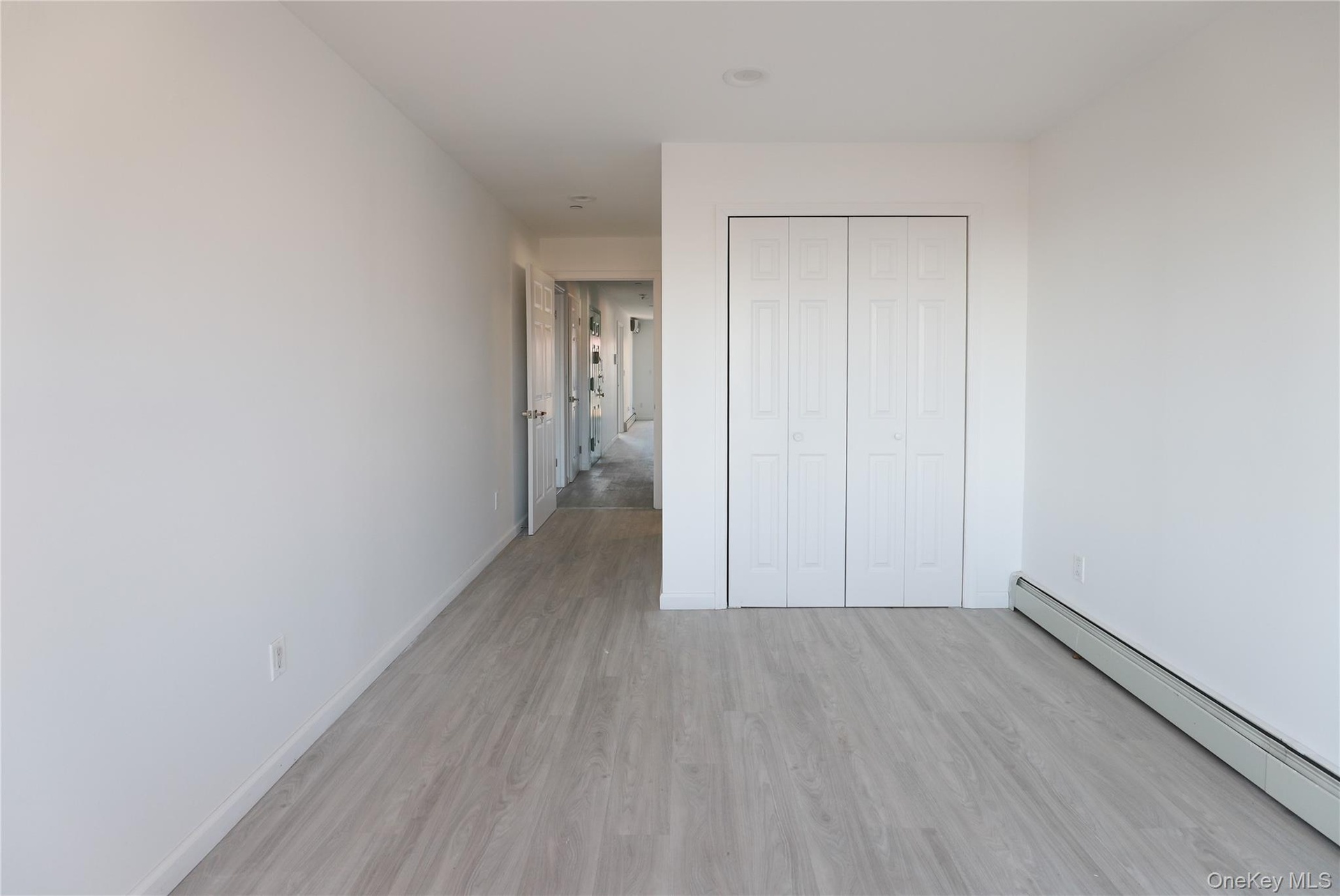 Neutral-toned interior featuring wood-finish flooring, white walls, and a built-in bifold closet