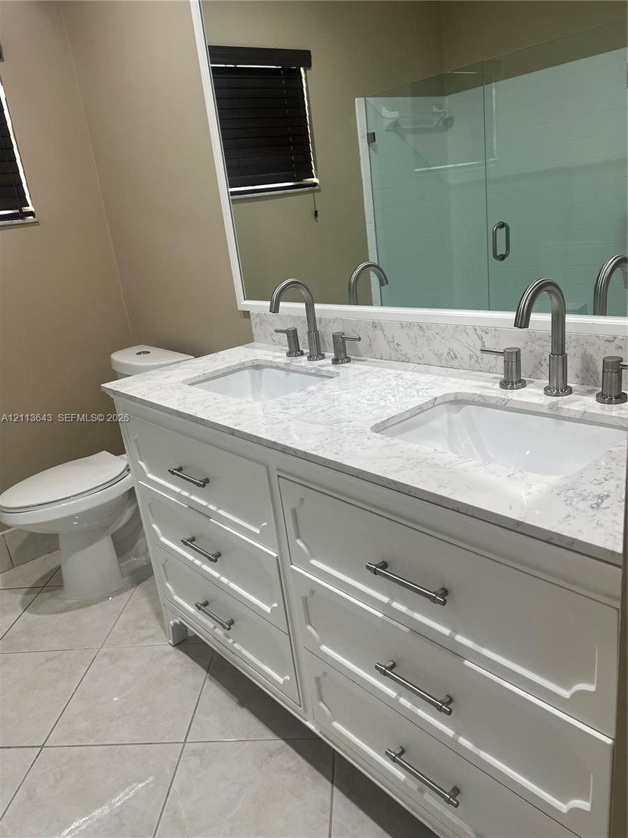 Dual-sink vanity with white cabinetry, light-toned stone-finish countertop, undermount rectangular sinks, brushed nickel hardware, and large wall-to-w