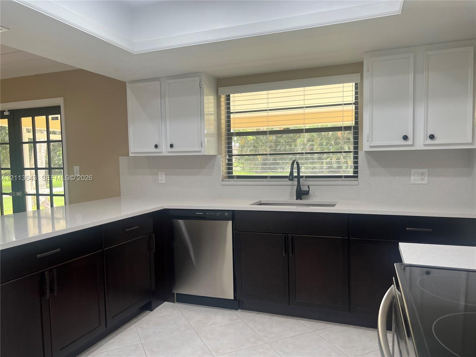 Kitchen featuringuu dual-tone cabinetry, stone-finish countertops, stainless steel dishwasher, undermount sink with a matte black faucet, and tile flo