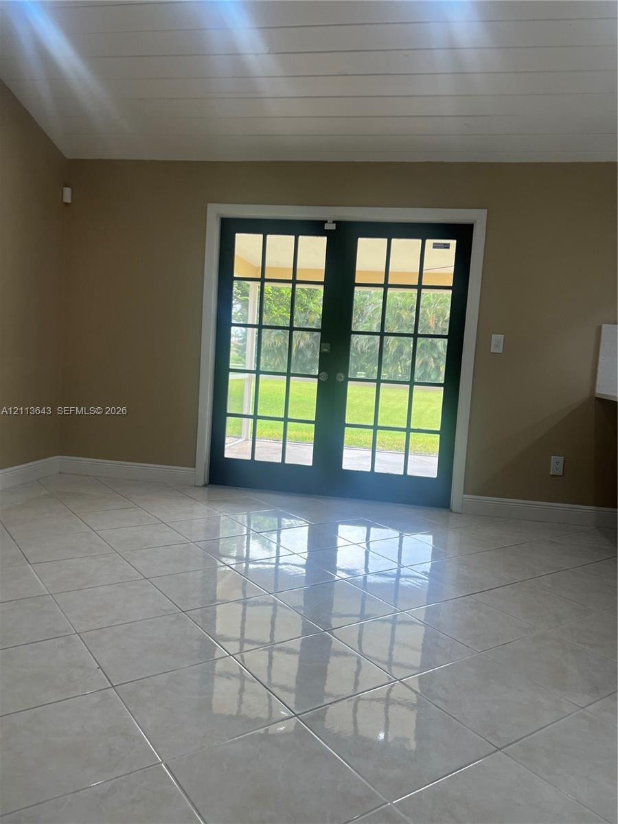 Double French doors featuring multi-pane glass, neutral tile flooring, and a vaulted ceiling with white paneled detail