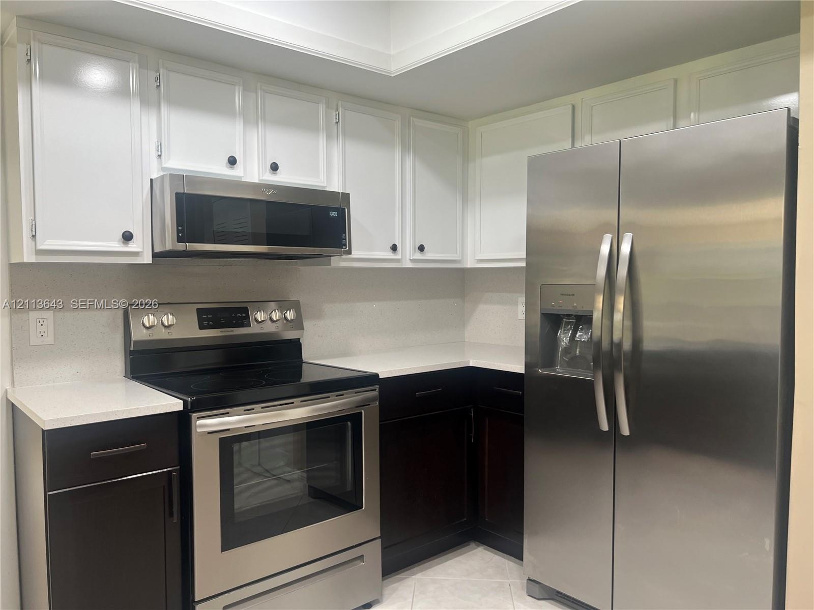 Kitchen featuring white upper cabinetry, dark lower cabinetry, light-toned stone-finish countertops, and stainless steel appliances including a range,