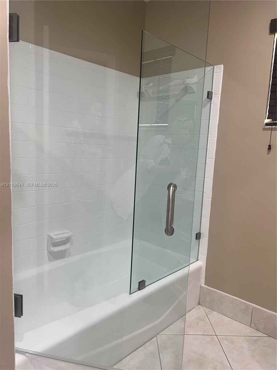 Bathtub featuring white tile surround, frameless glass door with brushed metal hardware, and integrated soap dish