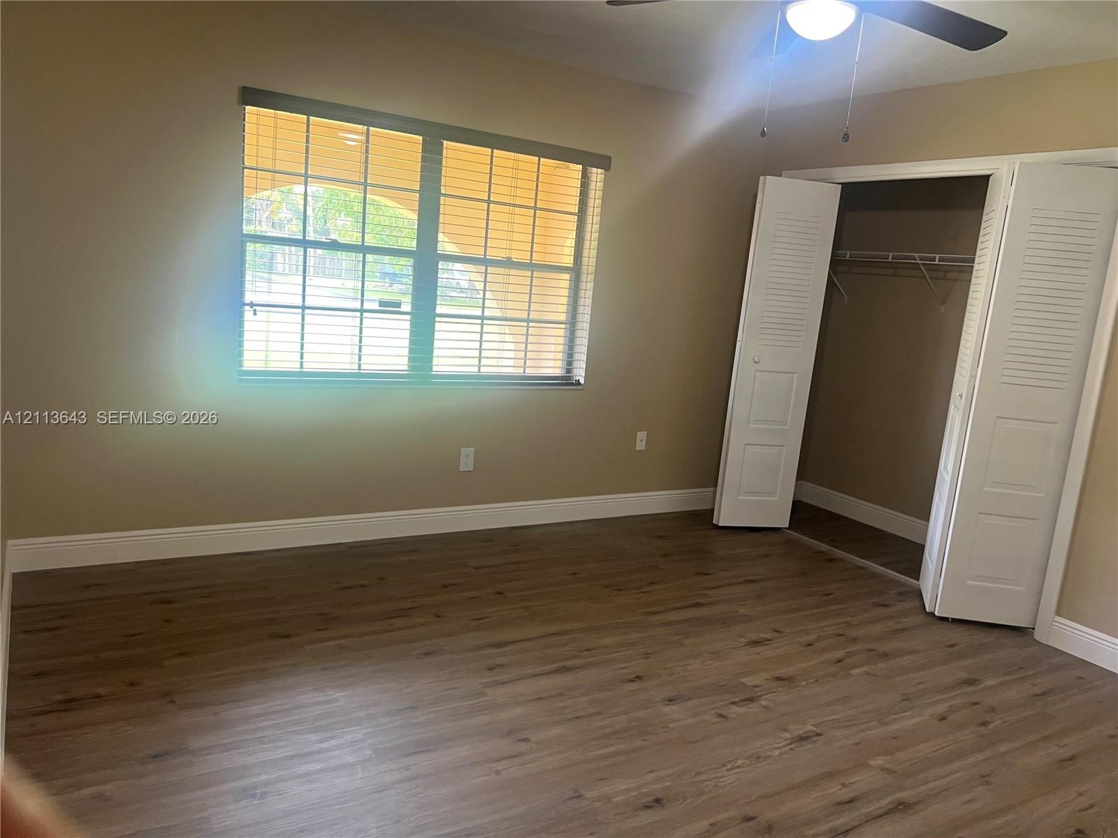 Wood-finish flooring, multi-pane window with blinds, ceiling fan, and built-in closet with louvered doors