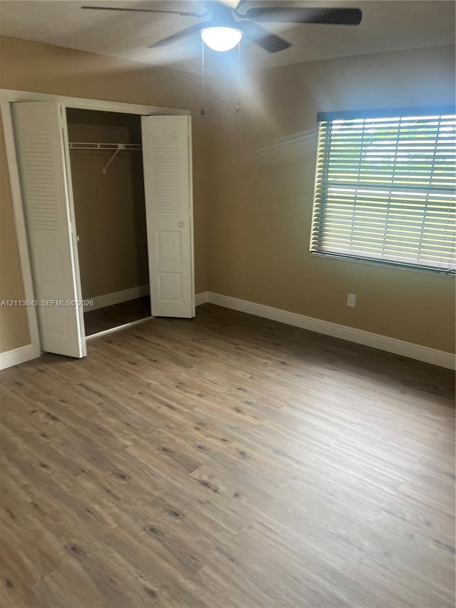 Interior space featuring wood-finish flooring, a ceiling fan with light fixture, a window with horizontal blinds, and a closet with bifold louvered do