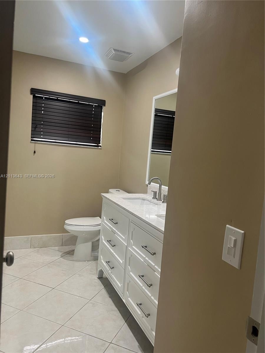 White shaker-style vanity with a stone countertop and rectangular undermount sink, complemented by diagonal-set floor tile and a framed wall mirror