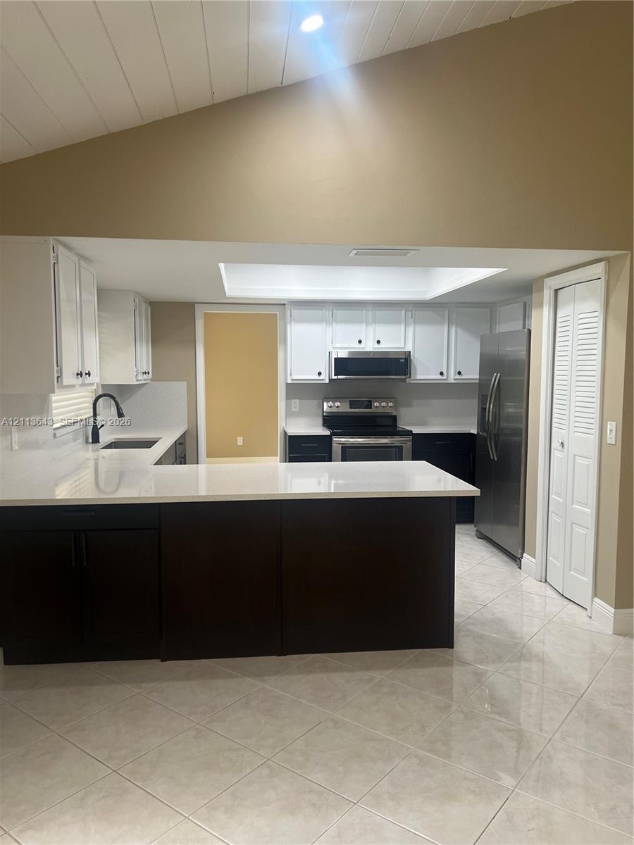 Kitchen featuring high-contrast white and dark cabinetry, quartz countertops, stainless steel appliances, a vaulted ceiling, and tile flooring