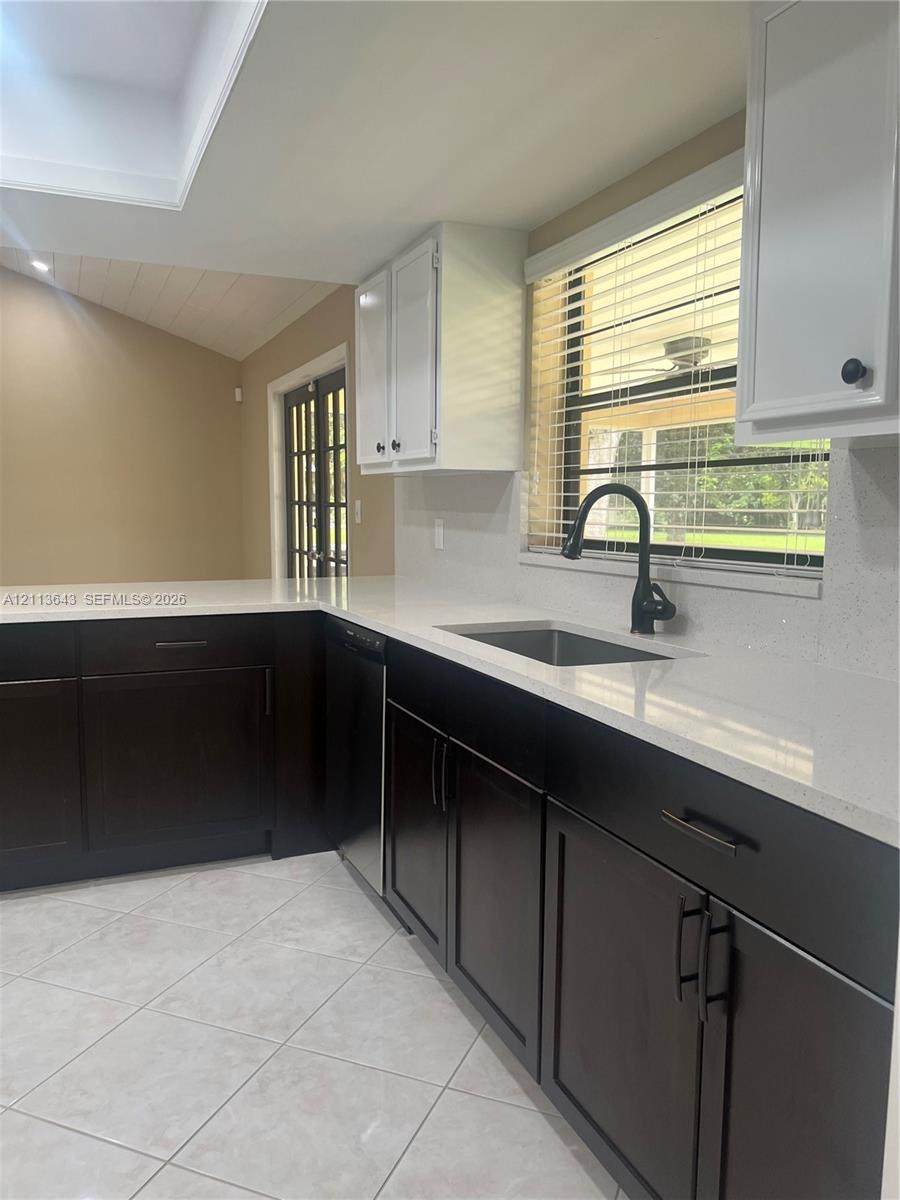 Kitchen featuring high-contrast cabinetry, stone countertops, stainless steel sink with matte black gooseneck faucet, tile flooring, and a glass-paned