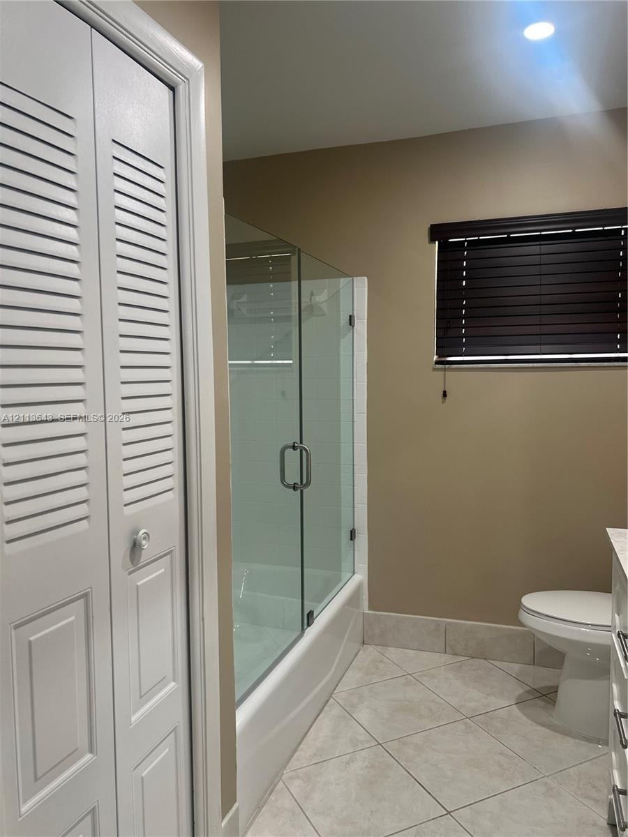 Full bathroom featuring a frameless glass shower enclosure, louvered closet doors, tiled flooring, and window blinds