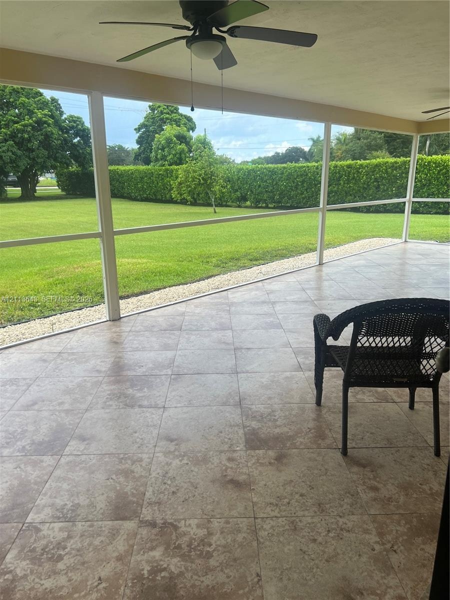 Screened lanai featuring large-format stone-look tile flooring, ceiling fans, and a expansive backyard with a manicured lawn and perimeter hedges