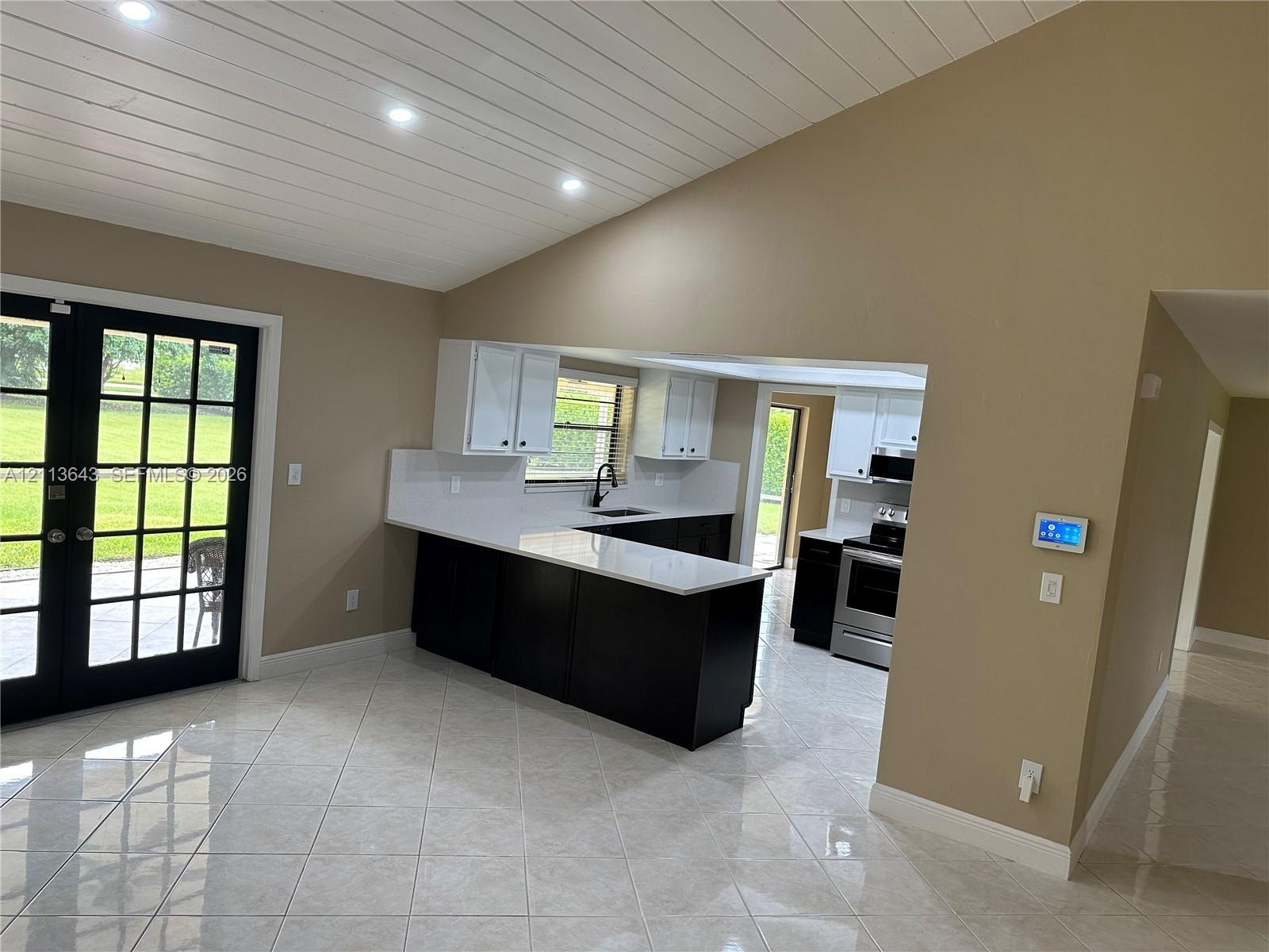 Kitchen featuring two-tone cabinetry, quartz countertops, tile flooring, vaulted ceiling with recessed lighting, and French doors