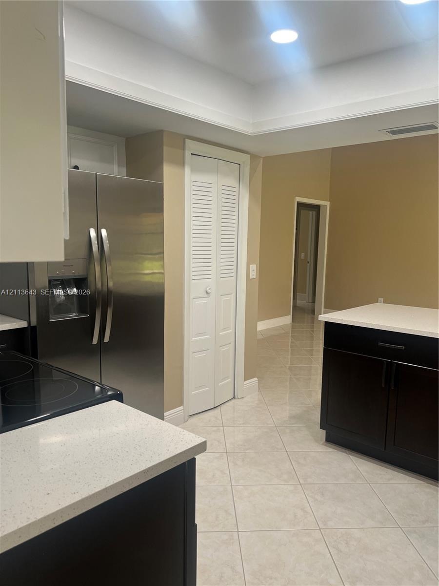 Kitchen featuring dark cabinetry, light-toned solid surface countertops, stainless steel side-by-side refrigerator, recessed lighting, and tile floori