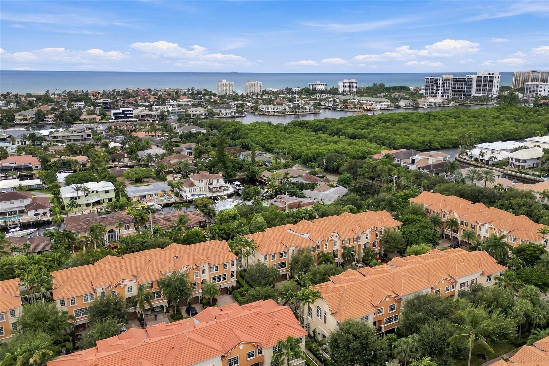 Aerial perspective of a multi-unit residential community featuring terra-cotta tile roofs, dense tropical landscaping, and proximity to coastal waterw