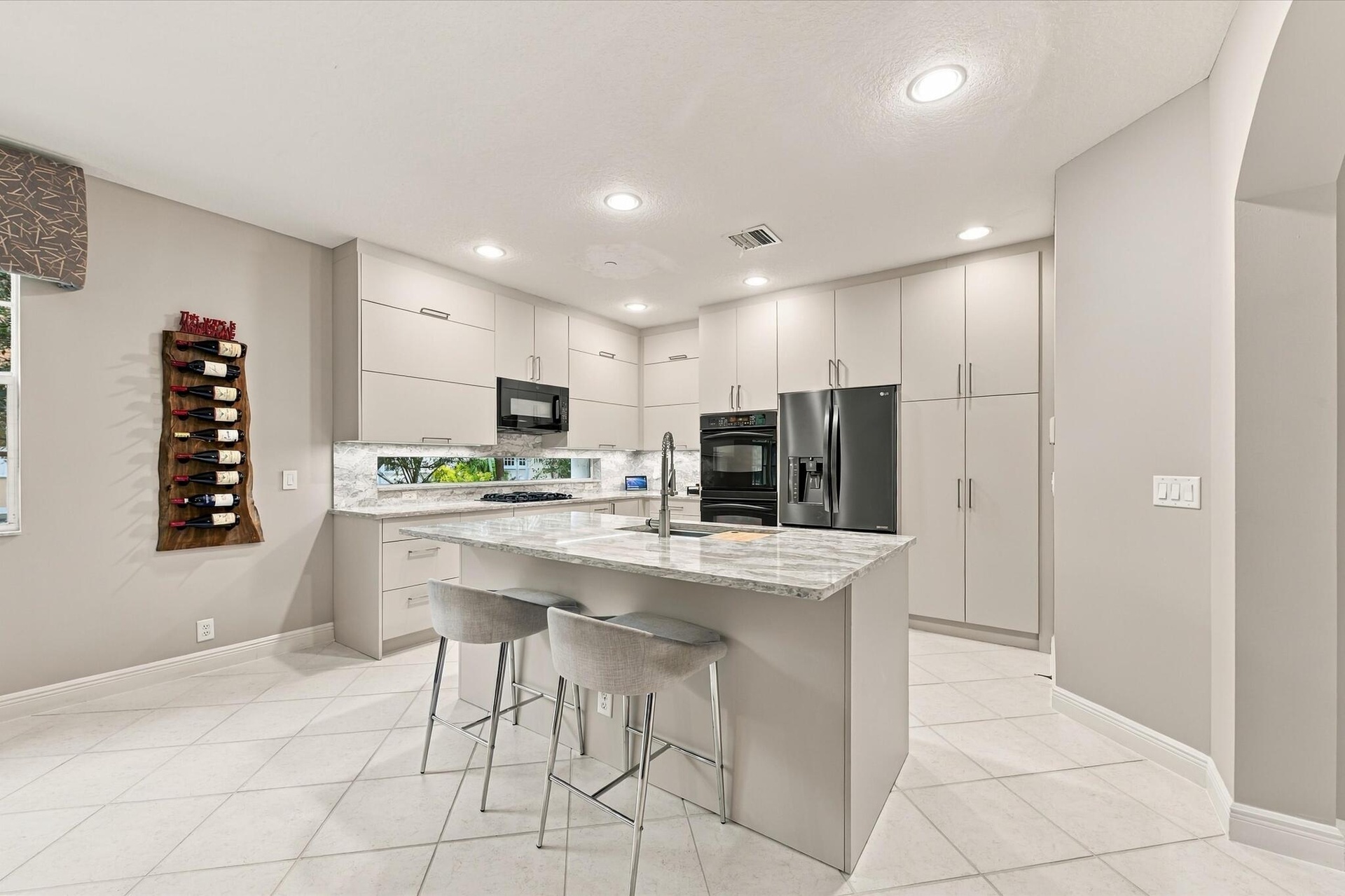 Kitchen featuring flat-panel cabinetry, quartz countertops, a central island with an integrated sink, built-in double wall ovens, and tile flooring