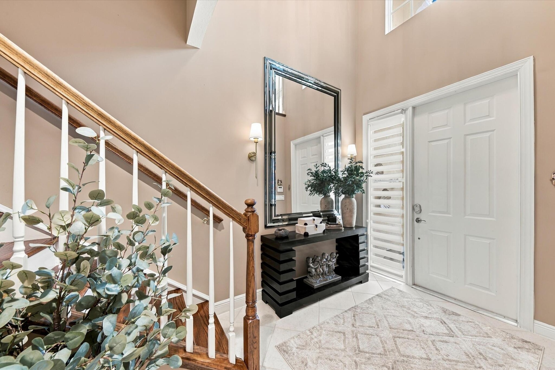 Foyer featuring a double-height ceiling, staircase with wood handrails and white balusters, multi-panel entry door with sidelight, tile flooring, and 