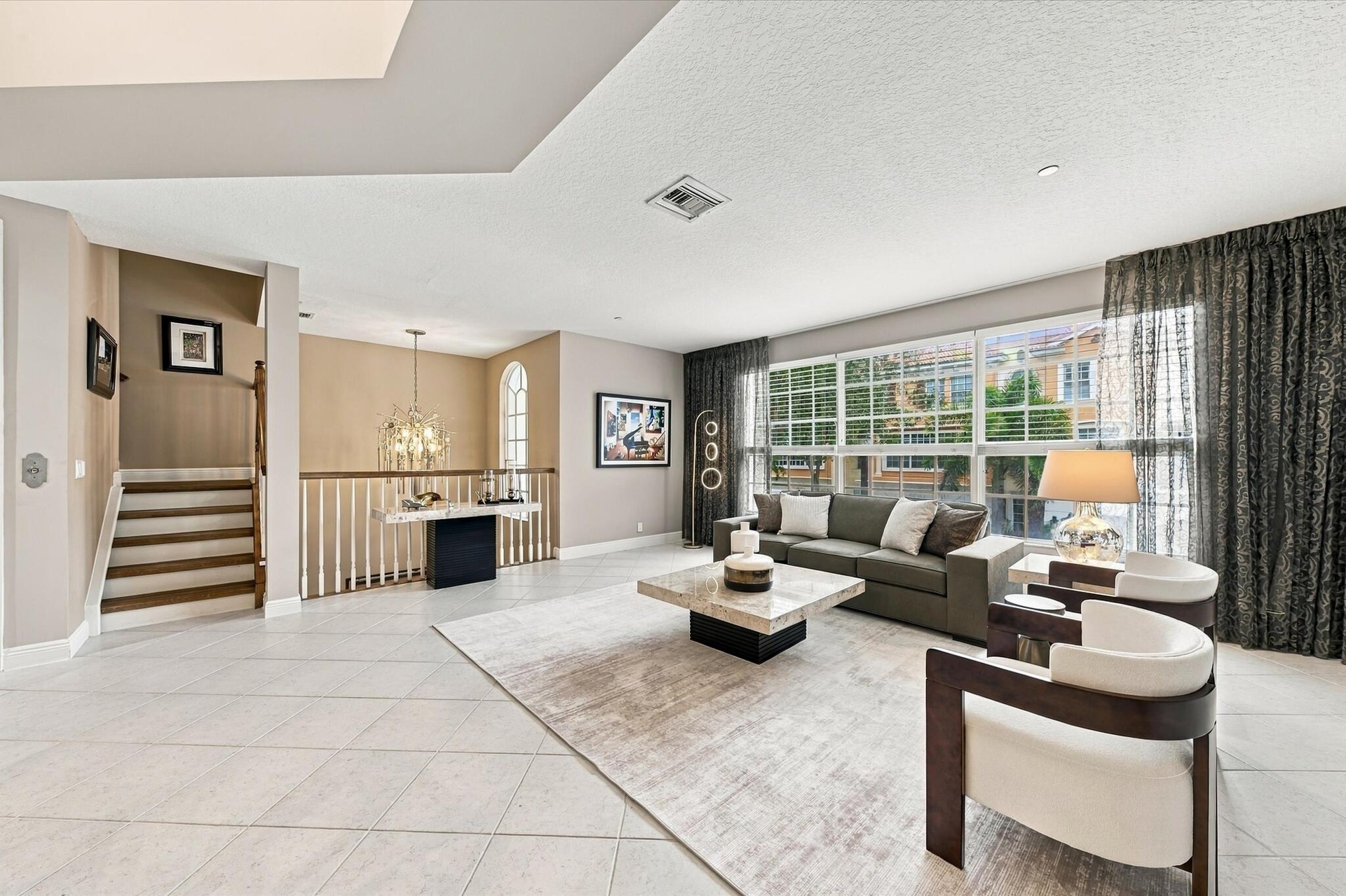 Open-concept interior featuring large-format tile flooring, multi-pane windows, arched window detail, and a staircase with wood treads and a baluster 