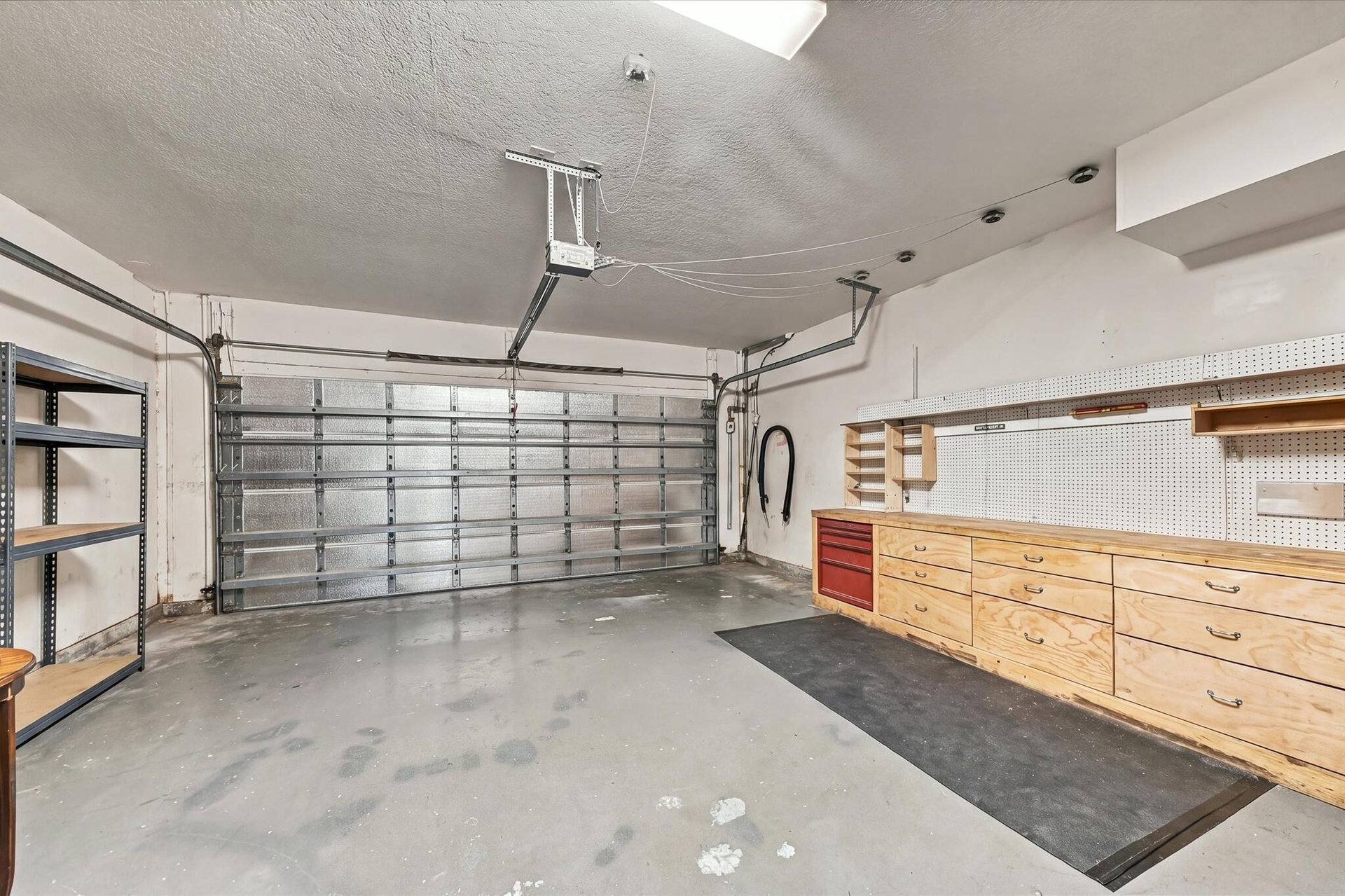 Attached two-car garage featuring a metal overhead door, custom built-in wood cabinetry, integrated pegboard wall organization, and finished concrete 