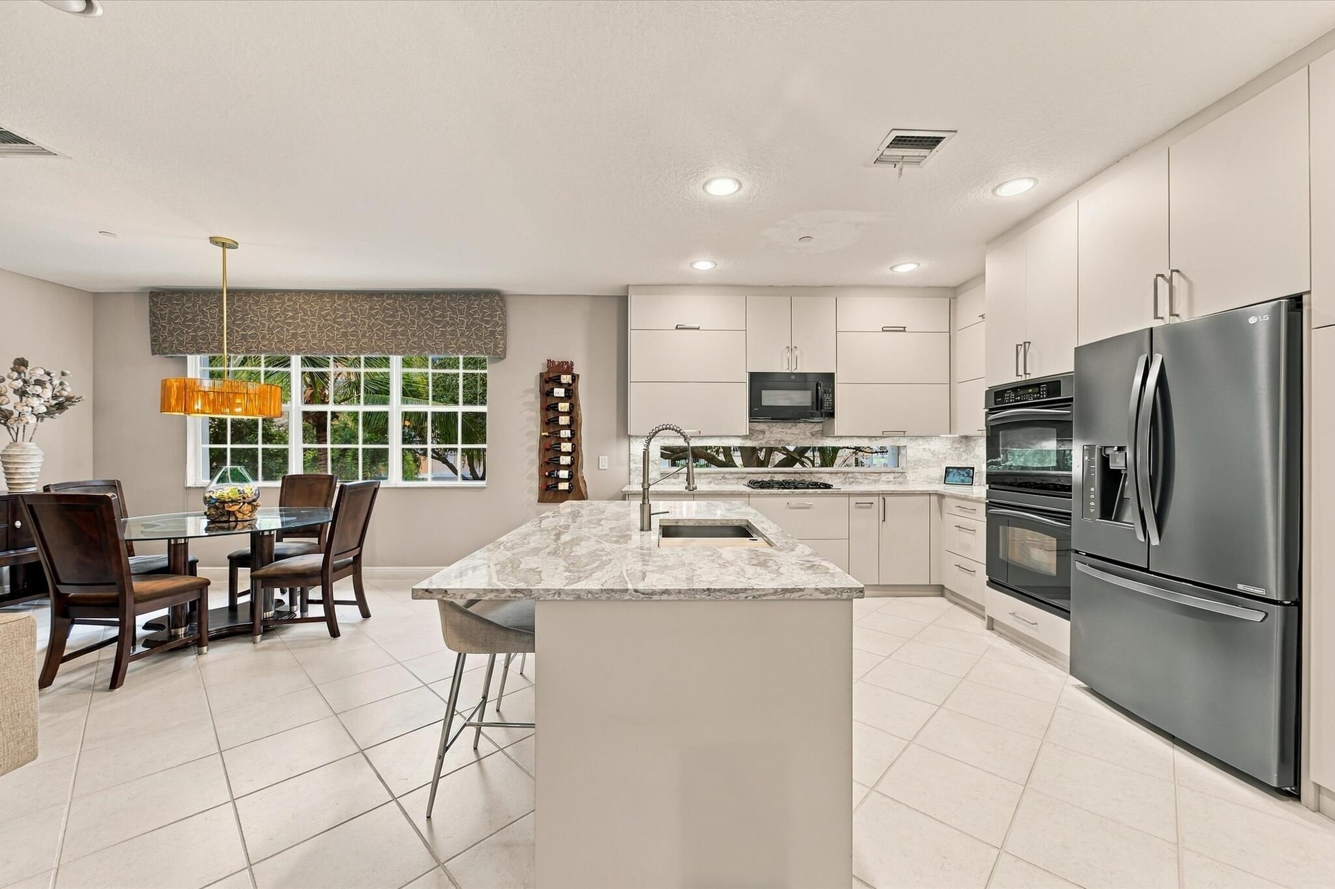 Kitchen featuring flat-panel cabinetry, a stone-surface island with an integrated sink, built-in stainless steel double wall ovens, a recessed microwa