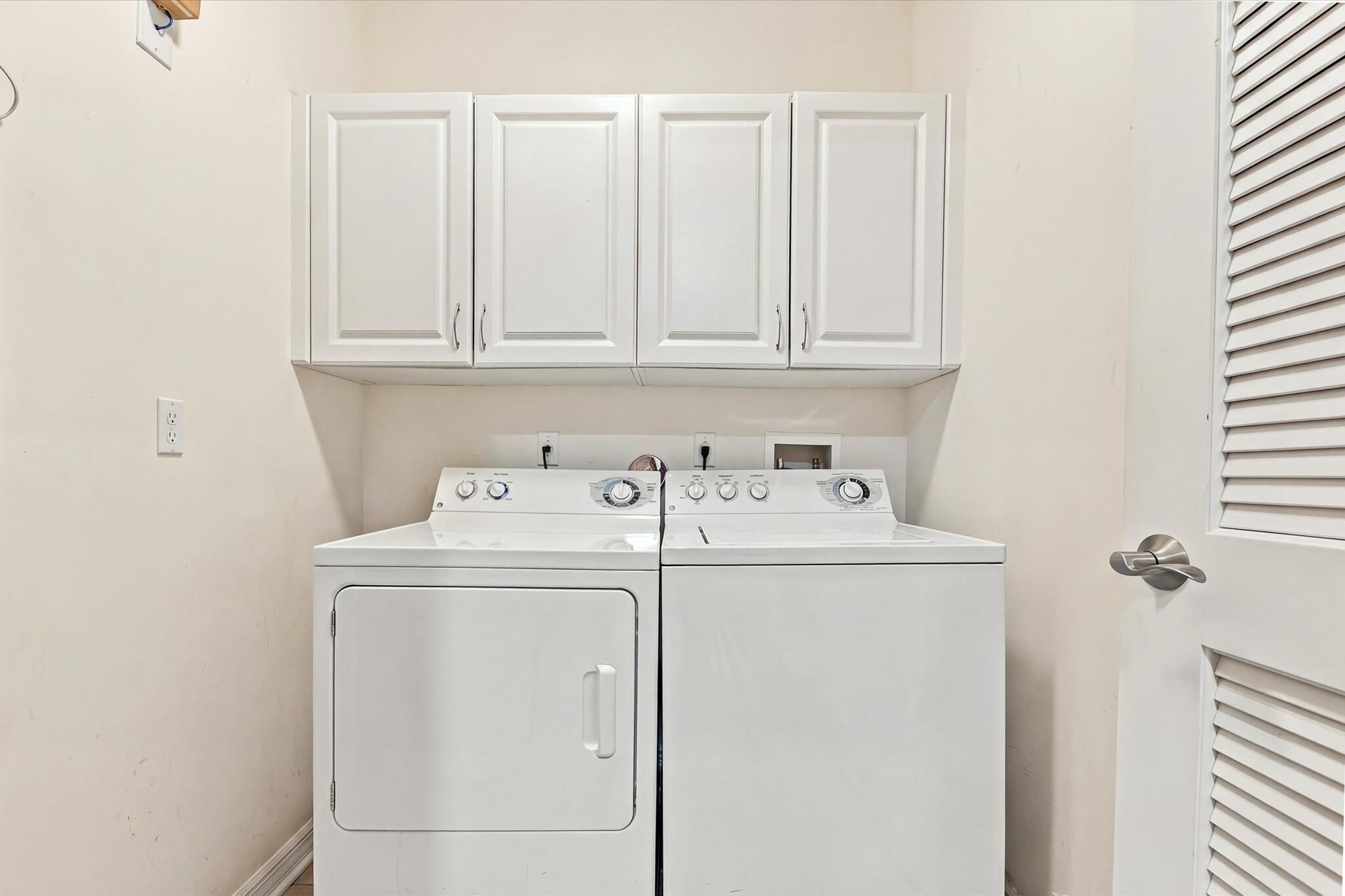 Laundry space featuring white upper cabinetry and a louvered door