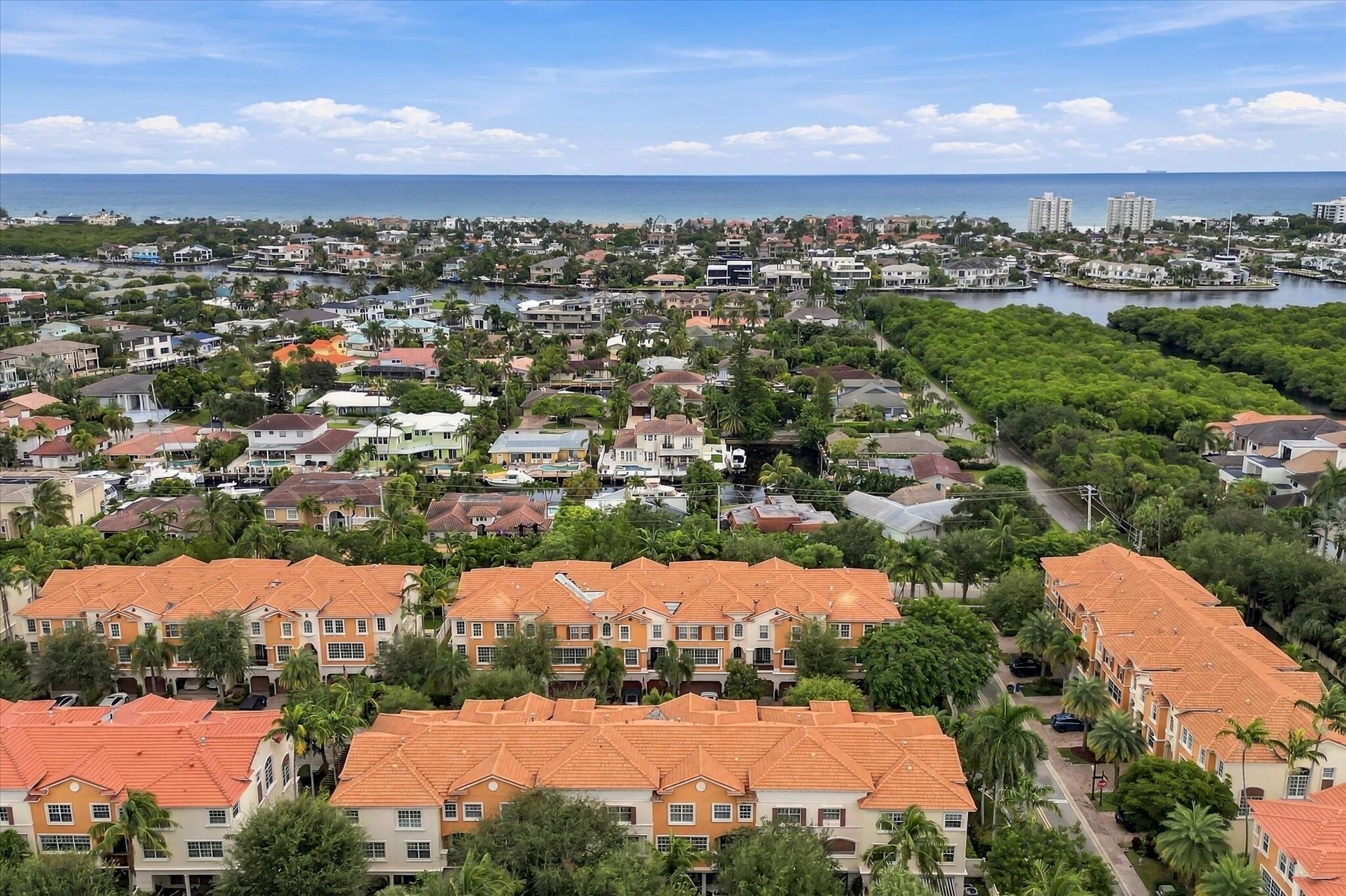 Aerial perspective of a multi-unit complex featuring terra-cotta tile roofs, stucco exterior finish, mature palm trees, and proximity to coastal water