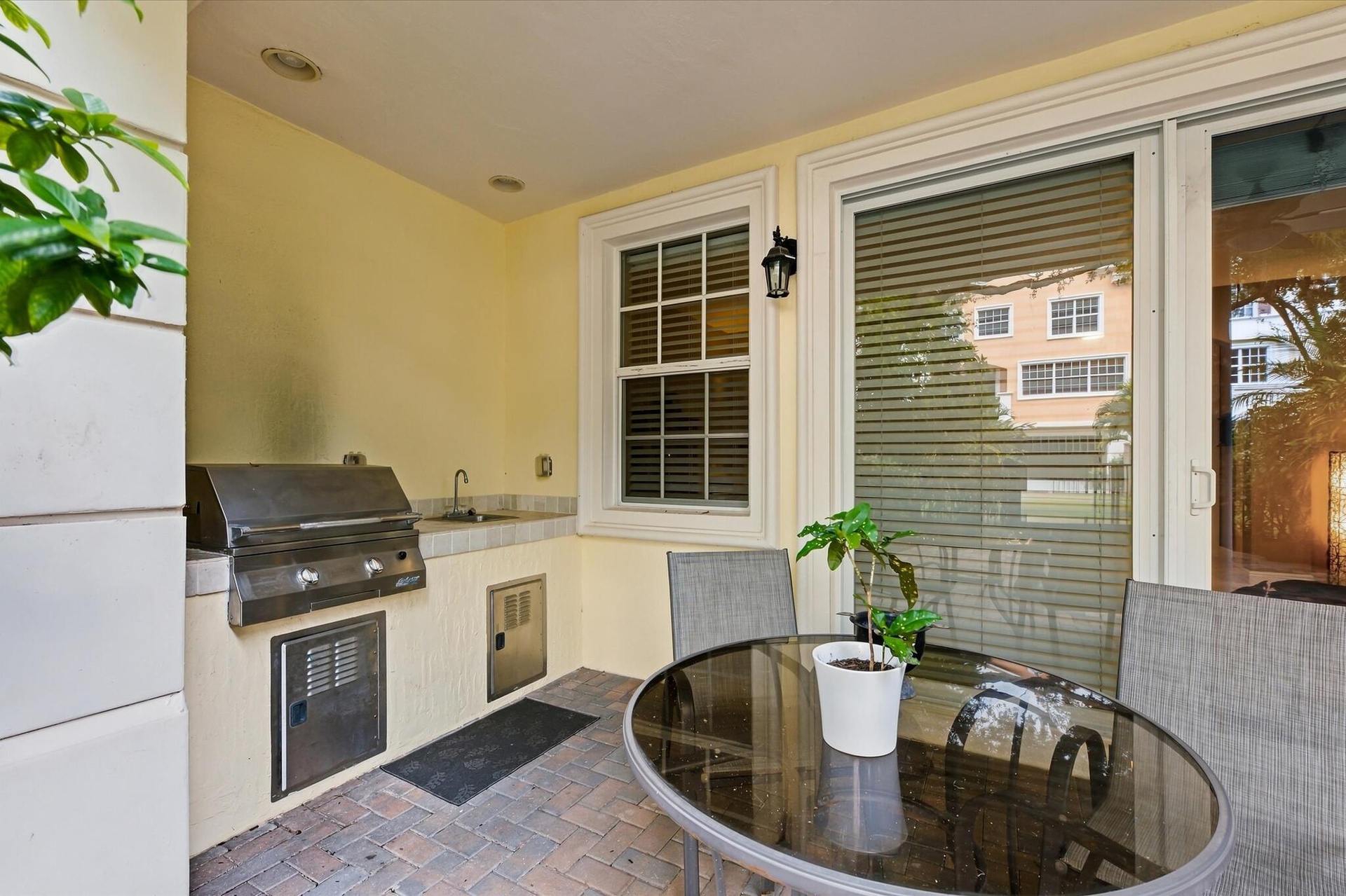 Covered outdoor kitchen featuring brick paver flooring, stainless steel built-in grill, stone-finish countertop, integrated sink, and recessed lightin