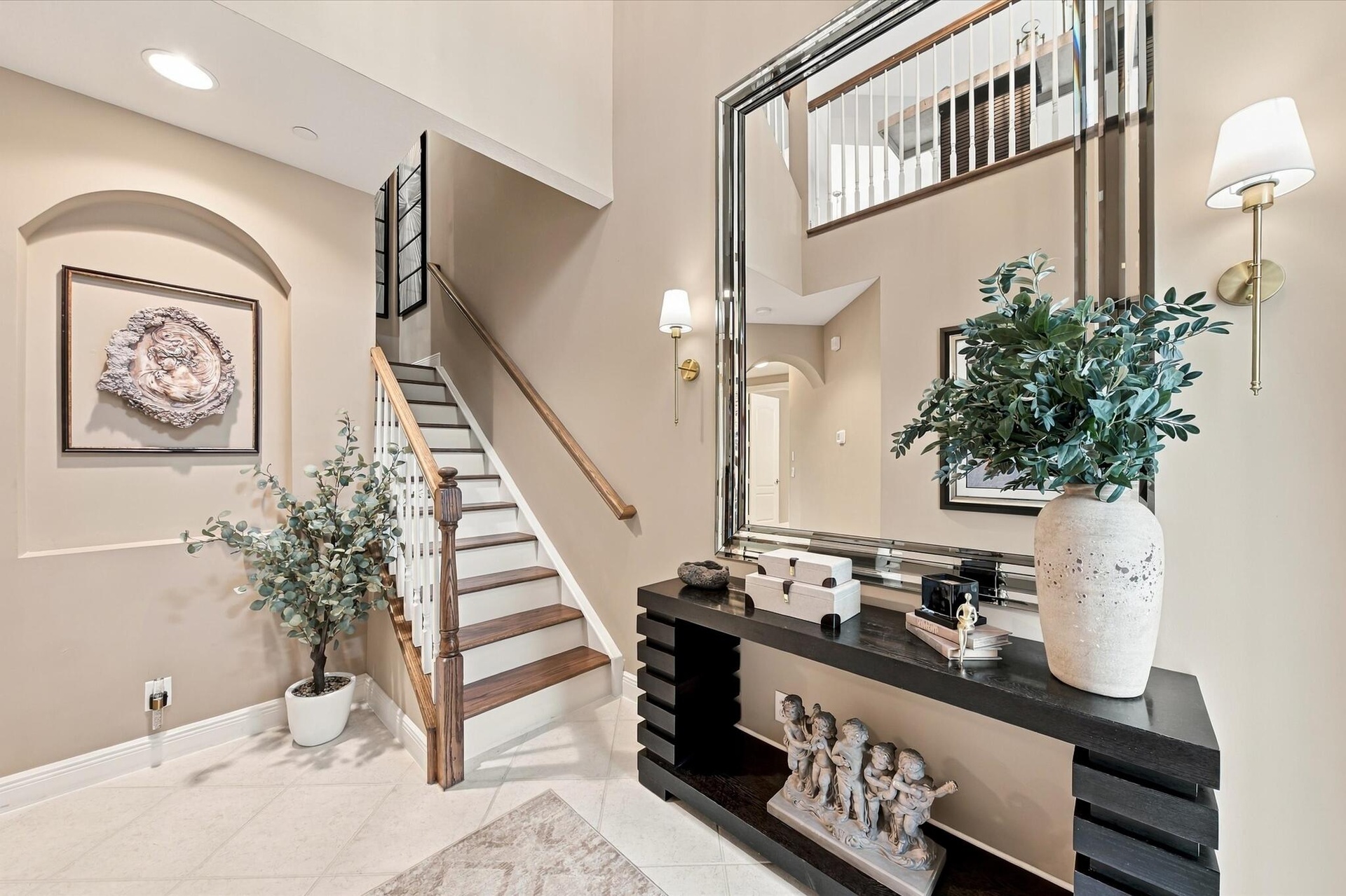 Two-story foyer featuring tile flooring, an arched recessed wall niche, a staircase with wood-finish treads and a white balustrade, and wall-mounted l