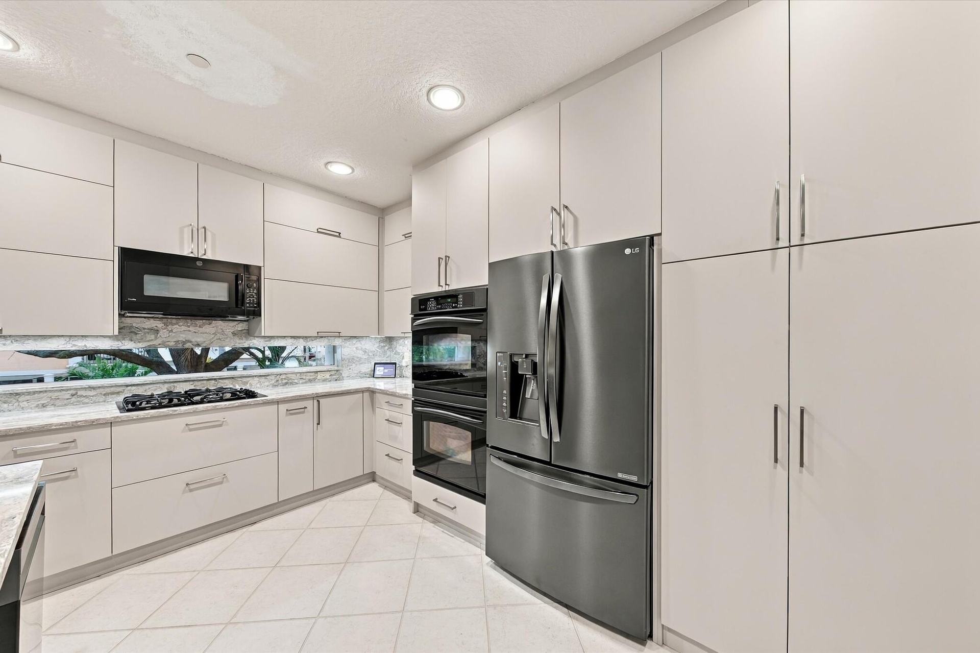Kitchen featuring flat-panel cabinetry, stainless steel wall-mounted oven and microwave, stainless steel French-door refrigerator, integrated cooktop,