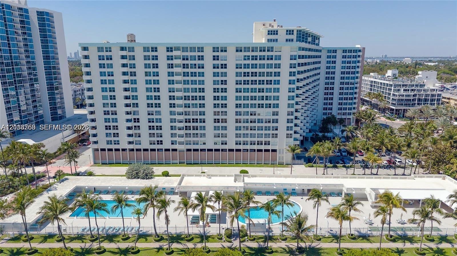 High-rise residential exterior featuring a multi-story facade, dual ground-level swimming pools, paved pool deck, and mature palm tree landscaping