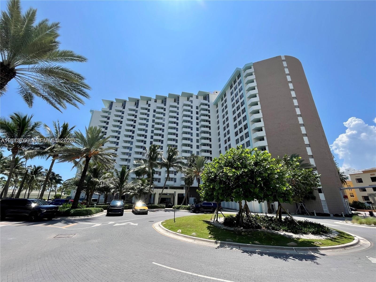 High-rise residential exterior featuring multiple tiers of private balconies, architectural concrete facade, circular paved motor court, and mature tr
