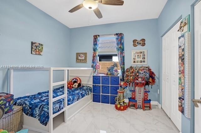 Room featuring polished stone-finish tile flooring, a centered ceiling fan with integrated light fixture, and double-door closet storage