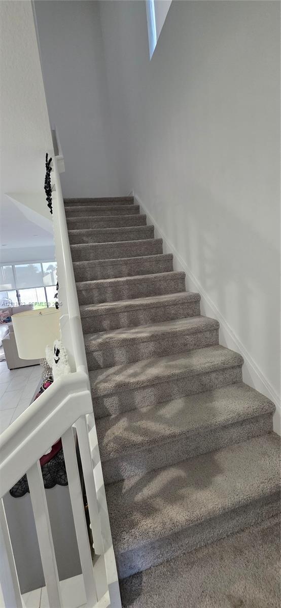 Staircase featuring wall-to-wall carpeting, white railing with vertical balusters, and high-reaching walls
