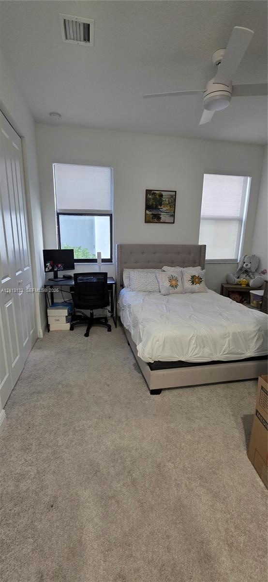 Room featuring wall-to-wall carpeting, dual windows with roller shades, a ceiling fan, and sliding closet doors