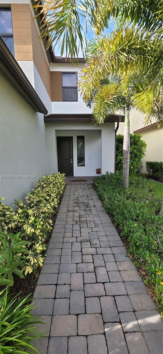 Paver walkway leading to a recessed entryway with a solid wood-finish door and exterior stucco facade