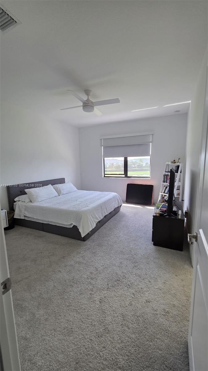 Neutral-toned wall-to-wall carpeting, ceiling fan with integrated lighting, and single-pane window with a roller shade