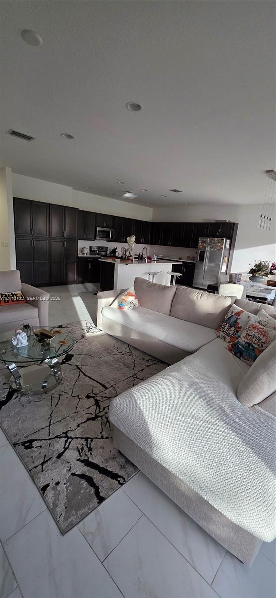 Open-concept area featuring large-format tile flooring, recessed ceiling lighting, and a kitchen equipped with dark cabinetry, a central island, and s