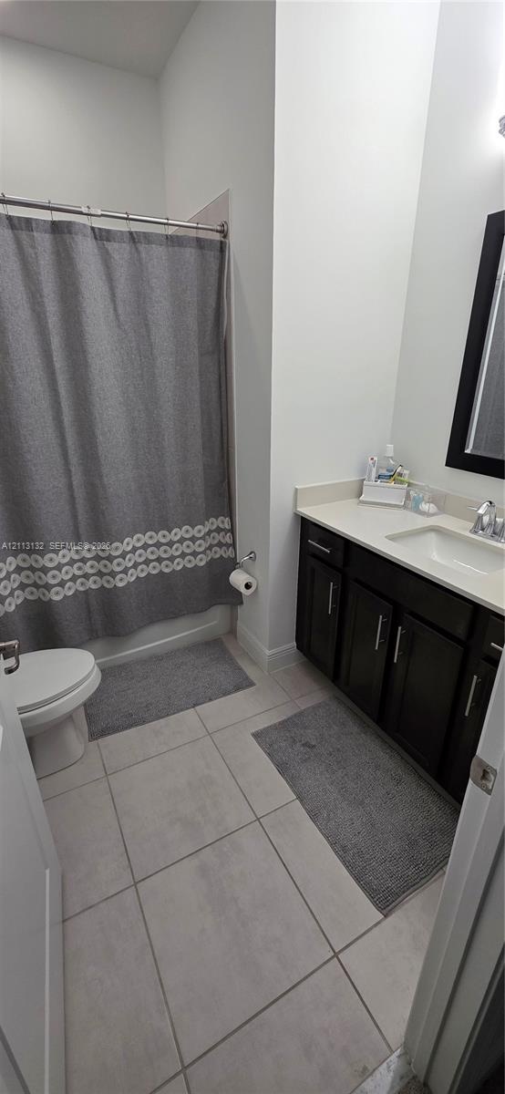Bathroom featuring dark wood-finish cabinetry, a light-toned solid surface countertop, rectangular under-mount sink, tiled flooring, and a shower-tub 